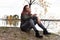 Woman in gray sits on stones by the lake in autumn