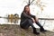 Woman in gray sits on stones by the lake in autumn