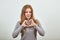 Woman in gray sweater smiles with happiness, showing hands the shape of heart