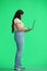 A woman, on a green background, in full height, uses a laptop, profile