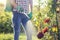 Woman in a green backpack with a pressure garden sprayer spraying flowers against diseases and pests