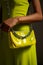 Woman in green dress holding yellow purse with chain. Generative AI