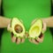 Woman in green shirt hands holding some avocados