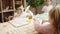 Woman and group of kids cutting paper sitting on table at kindergarten