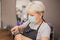 Woman hairdresser with face mask makes haircut using hair clipper and comb. Barber services with security measures from Covid-19.