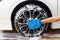 Woman hand with blue microfiber fabric washing wheel modern car or cleaning automobile.