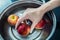 woman hand is cleaning red apple in bucket of water, closed up