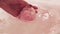 Woman hand dips a pink bath bomb in a warm bath.
