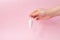 Woman hand folding white tampon on pink background, copy space