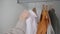 Woman hand hangs colored clothes on bar in white wardrobe