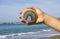 Woman hand hold pebble with painted rainbow against sea