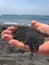 Woman hand holding black sand on the volcanic black sand beach