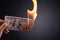 Woman hand holding burning burning dollar cash money over black background - business finances, savings and bankruptcy concept