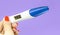 Woman hand holding digital pregnancy test isolated on purple. The pregnancy test screen with yes word.