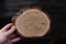 Woman hand holding empty circular piece of wood section texture on dark background. Copy space for text