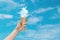Woman hand holding Ice cream cone with white cloud with blue sky in background.