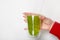 Woman hand holding kiwi smothie glass against white wall. Space for text