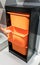 Woman hand holding orange plastic storage drawer in black cabinet against grey wall.