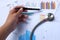 Woman Hand holding a pencil pointing to the graph document on the doctor`s desk with stethoscope.