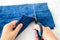 Woman hand holding a scissors and cutting out a folded in half blue jean shorts. Shorten the denim shorts with scissors and sewing