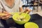 Woman hand holding a thick slice of boiled pork with green plastic chopsticks over a bowl of thai pork noodle soup