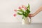 Woman hand holding watering can with bouquet of tulips on beige background. Spring home interior decoration, slow living, mental