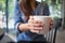 Woman hand holding white coffee cup. Mock up, perfect for putting your design on. Young Asian girl sitting at table with laptop