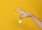 Woman hand holds hanging key on iron ring on yellow background with his fingers.