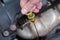 Woman hand holds metal oil dipstick with yellow handle extended from socket, under hood of car against background of engine body.