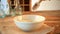 Woman hand is pouring dry quinoa grains with scoop on wooden kitchen table.