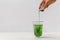 Woman hand pouring liquid chlorophyll in a glass cup. White background