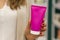 Woman hand with purple cream tube in a bright store background