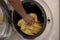 Woman hand put yellow towel into washing machine. Housewife work laundry at home