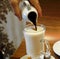 A woman hand is putting coffee to the hot milk on a glass cup.