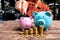 Woman hand putting gold coin into pink piggy bank with golden coins growth bar graph, step up growing business to success and