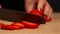 Woman hand with red nails, slicing whole piece of fresh strawberry, laying on wood table, wood texture cutting board,