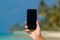 Woman hand showing a blank smart phone on the beach with the sea