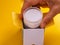 A woman hand taking face cream out of a box on yellow background