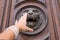 Woman hand touching old wooden door with lion head copper knoc