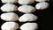 Woman hands baker put dough in the form of elongated round balls in a row on black baking sheet, close up view homemade