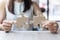 Woman hands connecting couple puzzle over table, businesswoman holding wood jigsaw inside office. Business solutions, mission,