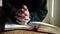 Woman with hands crosses on top of bible in prayer posture.