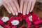Woman hands with french nails polish style and wooden bowl with water and floating candles and red rose petals