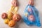 Woman hands hold mixed organic fruit, vegetables and greens in a string bag and plastic on light background. Zero waste