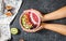 Woman hands hold raspberries smoothie bowl with figs, kiwi and coconut on concrete background