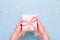 Woman hands holding gift box in pink color on pastel blue background with heart shape confetti, copyspace. Valentine`s Day