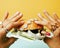 Woman hands holding hamburger with money, jewelry, cosmetic, social issue wealth concept close up