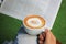 Woman hands holding hot cups of coffee with milk foam and newspaper in morning on green background