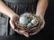 Woman hands holding marble Easter eggs with feathers on dark background with light. Happy Easter holiday, selective focus.