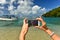 A woman hands holding mobile take photo of paradise beach.